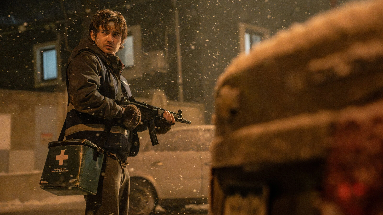 Austin Abrams holding a gun, carrying a medical courier bag in a snowy city.