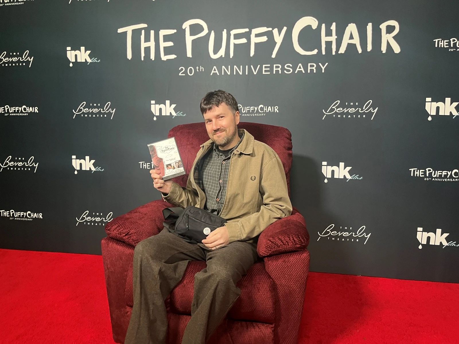 Slowburn contributor at sitting in a replica of the red puffy chair from the film, which is set up on a red carpet photo area in front of the theater.